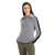 A woman stands with her hands in her pockets against a white background, wearing the Icebreaker Womens Lodge LS Half Zip Sweater with a zip collar and black sleeve stripes, paired with olive green cargo pants.