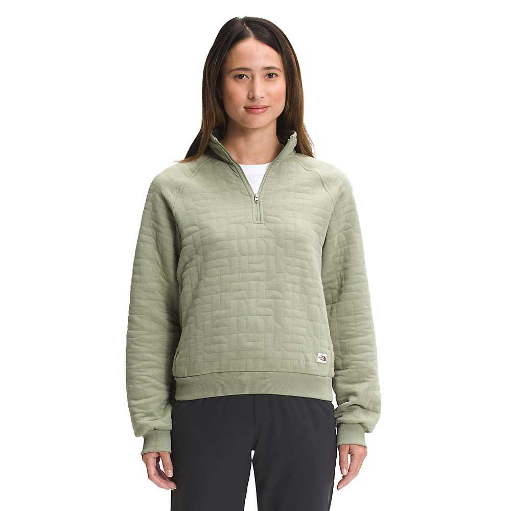 A woman faces forward, wearing The North Face Women's Longs Peak Quilted 1/4 Zip Jacket in light green with black pants, set against a plain white background.