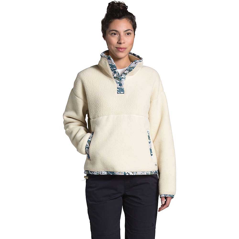 A woman in The North Face Women's Liberty Cragmont Fleece 1/4 Zip Top, featuring Liberty print trim, dark pants, and a bun hairstyle stands with one hand in her pocket against a plain white background.