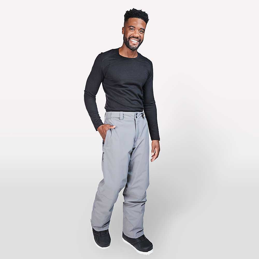 A man smiles while posing in a black long-sleeve shirt, Moosejaw Men's Insulated Ski and Snow Pant, and black boots, standing against a white background.