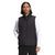 A person with long dark hair wears The North Face Men's Junction Insulated Vest in black over a white long-sleeve shirt and black pants, standing against a plain white background.