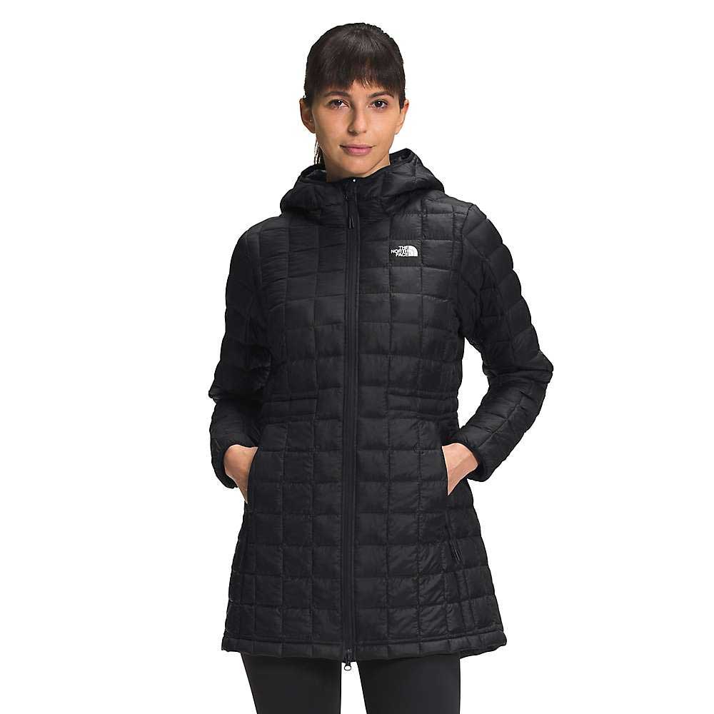 A woman stands facing the camera, hands in her pockets, wearing The North Face Womens ThermoBall Eco Parka—a long black insulated jacket with a hood, front zipper, left chest logo, and recycled nylon construction.