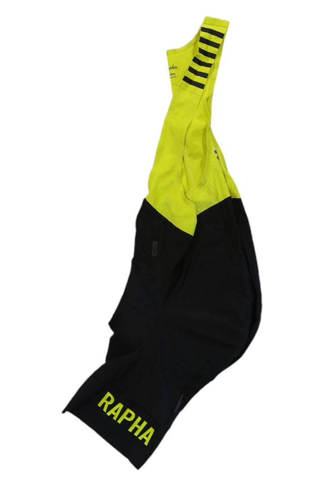The Rapha Mens Pro Team Bib Shorts II - Regular feature a bright yellow upper, black lower section, RAPHA in yellow on the left leg, black stripes on the left shoulder strap, and a race-grade chamois for comfort.