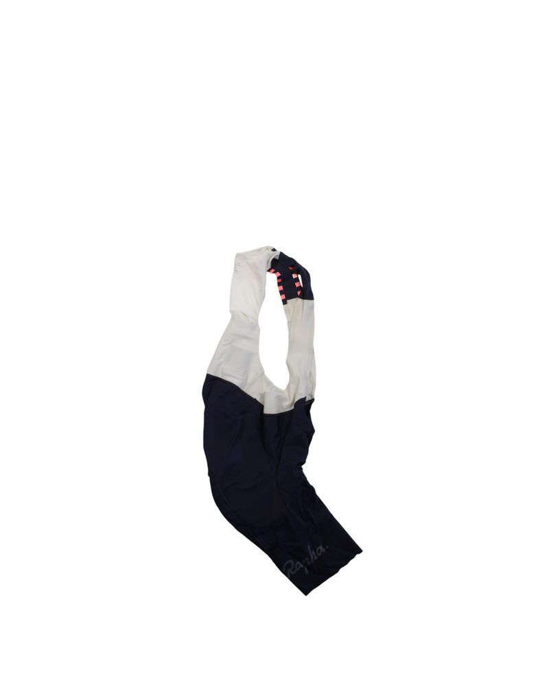 Rapha Mens Pro Team Bib Shorts II - Regular in navy blue and white, featuring a race-grade chamois and red-white checkered strap detail, shown against a plain white background.