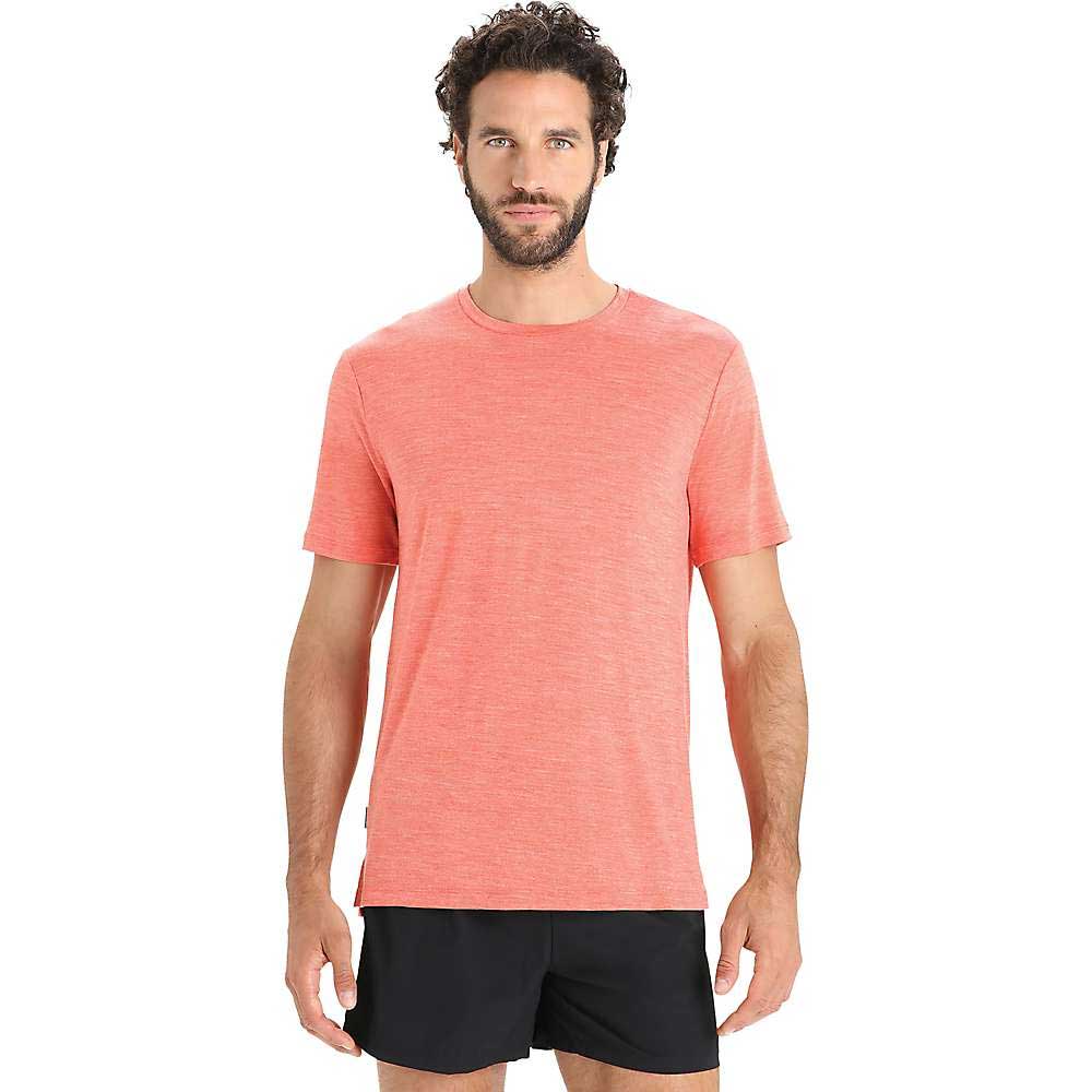 A man with curly dark hair and a beard wears the Icebreaker Mens Sphere II SS Tee in pink and black shorts, standing against a plain white background.