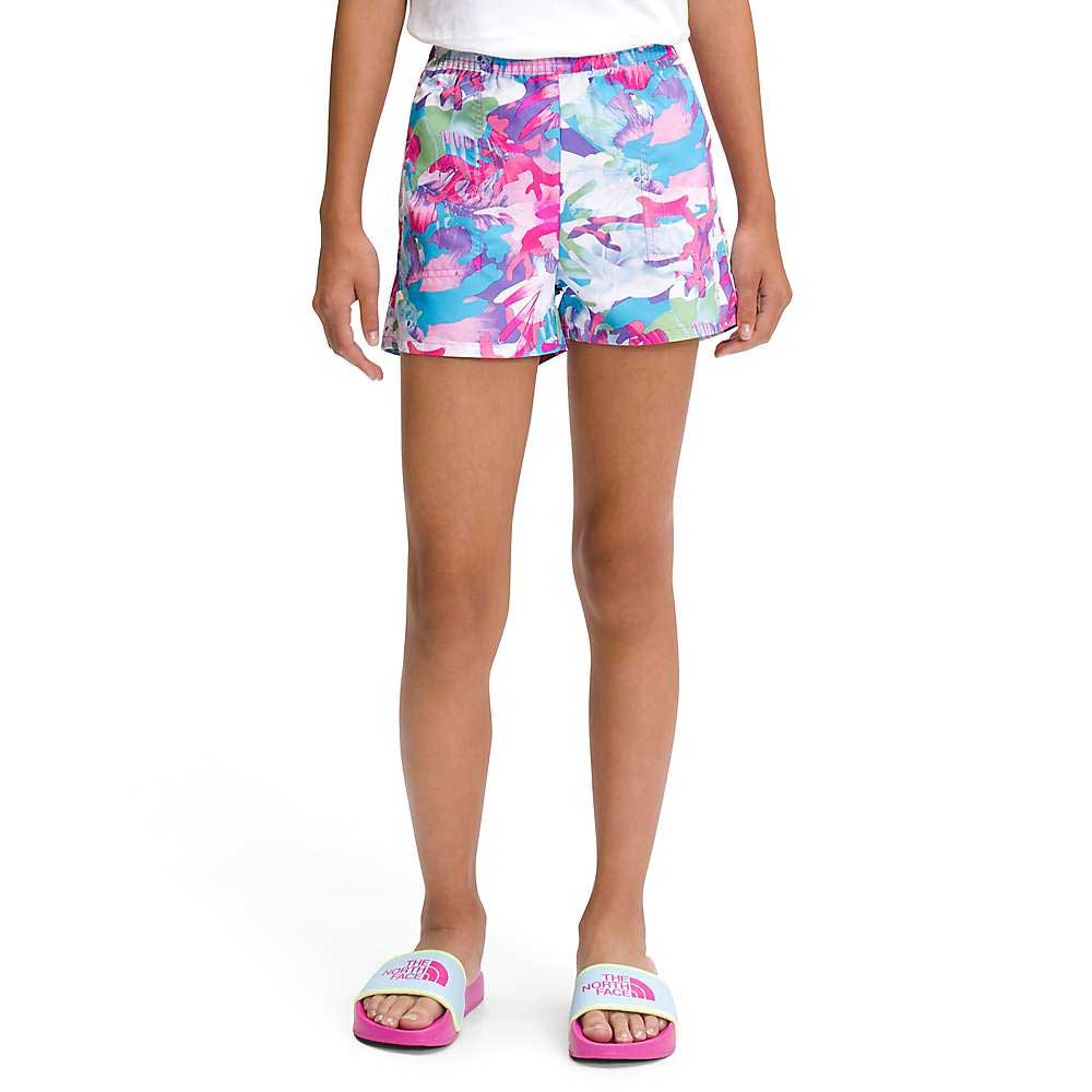 A person wearing The North Face Girls Printed Amphibious Class V Water Short in pink, blue, and white, a white top, and white slide sandals with pink soles stands against a plain white background.