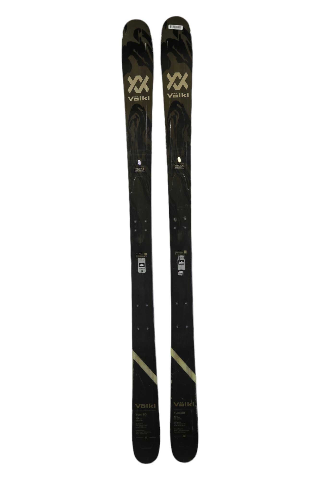 A pair of Volkl Yumi 80 black women's skis with gold and silver accents stand upright side by side on a white background—perfect all-mountain skis.
