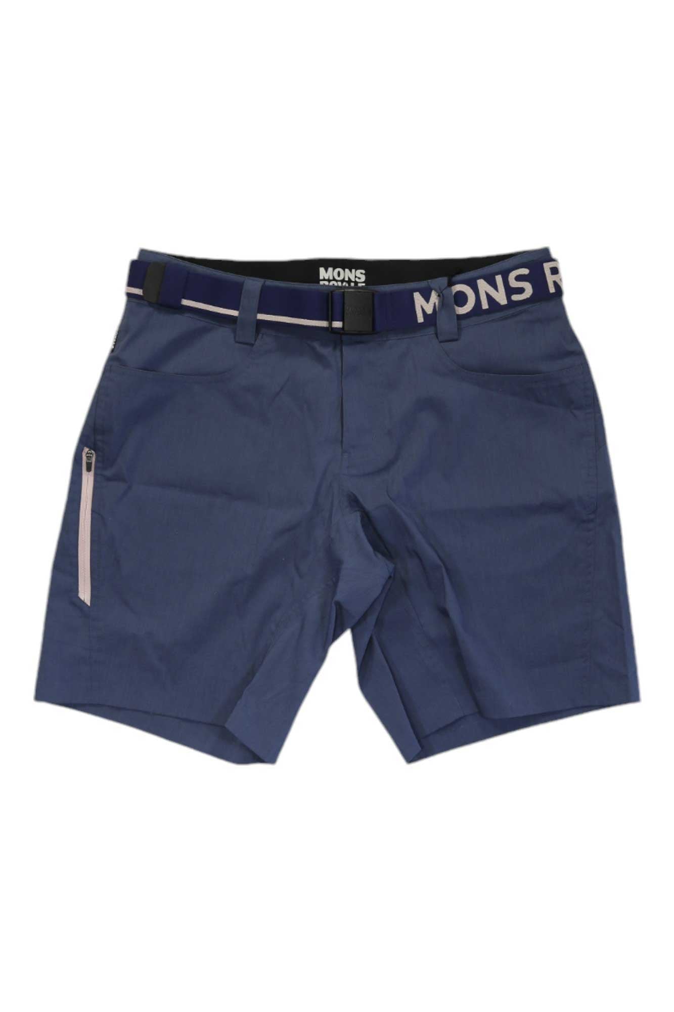Blue Mons Royale Womens Nomad Shorts with front pockets, a left zippered pocket, belt loops, and a navy belt with white MONS text. Tailored fit and Merino Wool blend make them perfect for hiking adventures.
