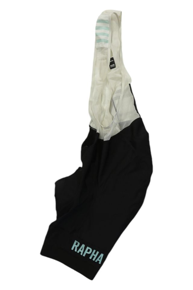 Rapha Mens Pro Team Bib Shorts II - Regular in black with white mesh shoulder straps and light blue RAPHA text on the left leg, featuring a race-grade chamois. Bib shorts are displayed flat on a white background.