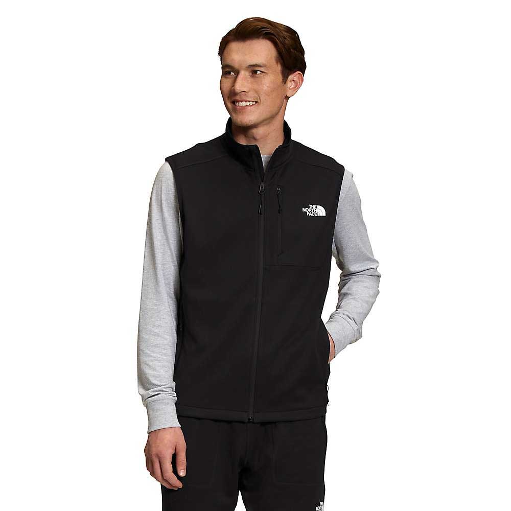 A man wearing The North Face Mens Canyonlands Vest over a light gray long-sleeve shirt stands with one hand in his pocket, smiling and looking to the side against a white background.