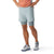 A person in a peach athletic shirt, Smartwool Men's Intraknit Active Lined 5 Inch Shorts in light gray, and light gray athletic shoes stands hands on hips against a white background.