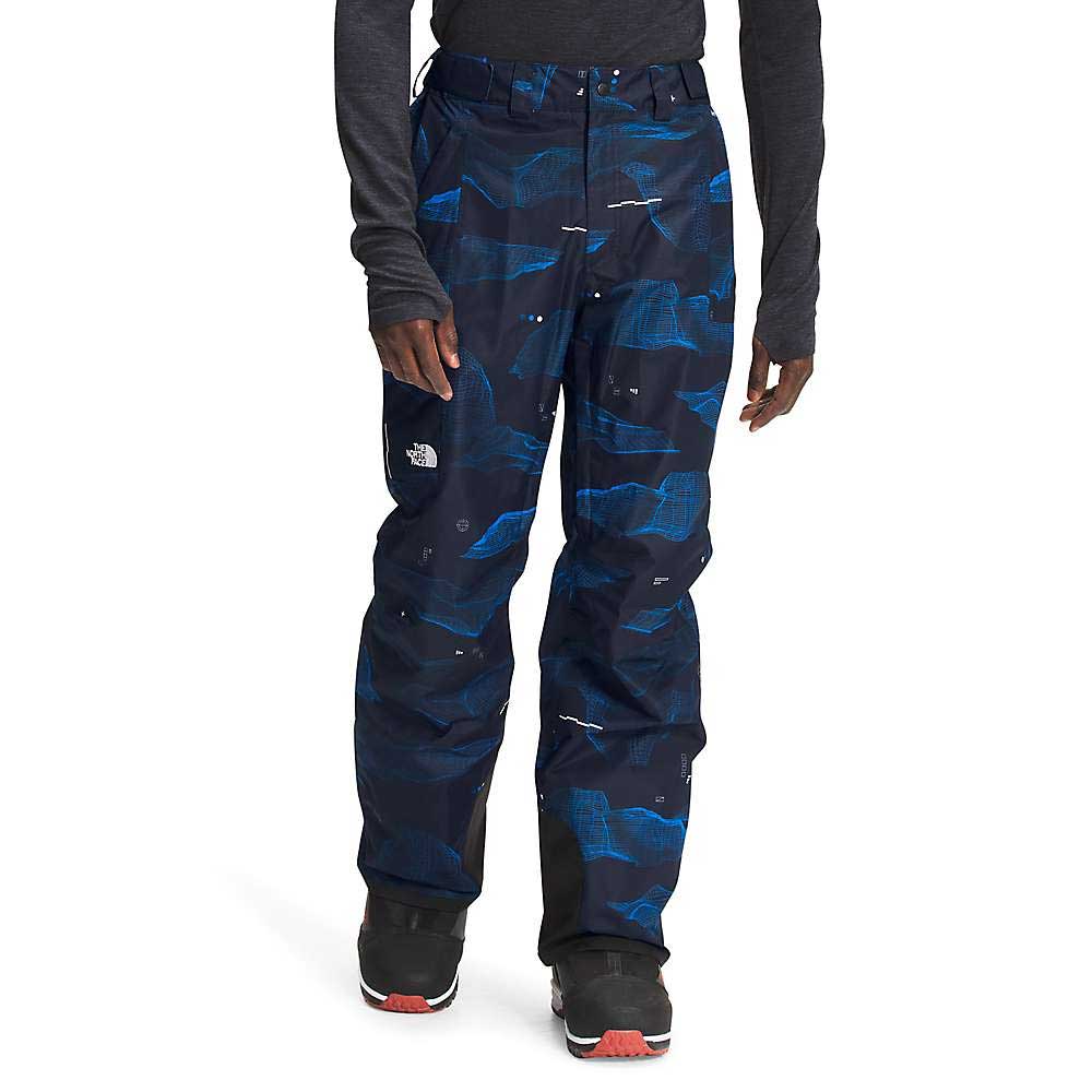 Wearing The North Face Mens Freedom Pant—dark pants featuring blue geometric patterns, water-resistant DryVent fabric, and a logo on one leg—paired with a long-sleeve shirt and black boots with red soles.