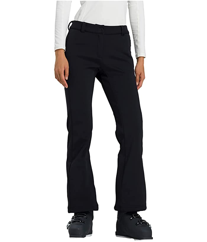 A woman stands against a plain background, wearing Rossignol Womens Softshell Ski Pants, black boots, and a white long-sleeve top. The photo highlights the winter sports pants from waist to feet.