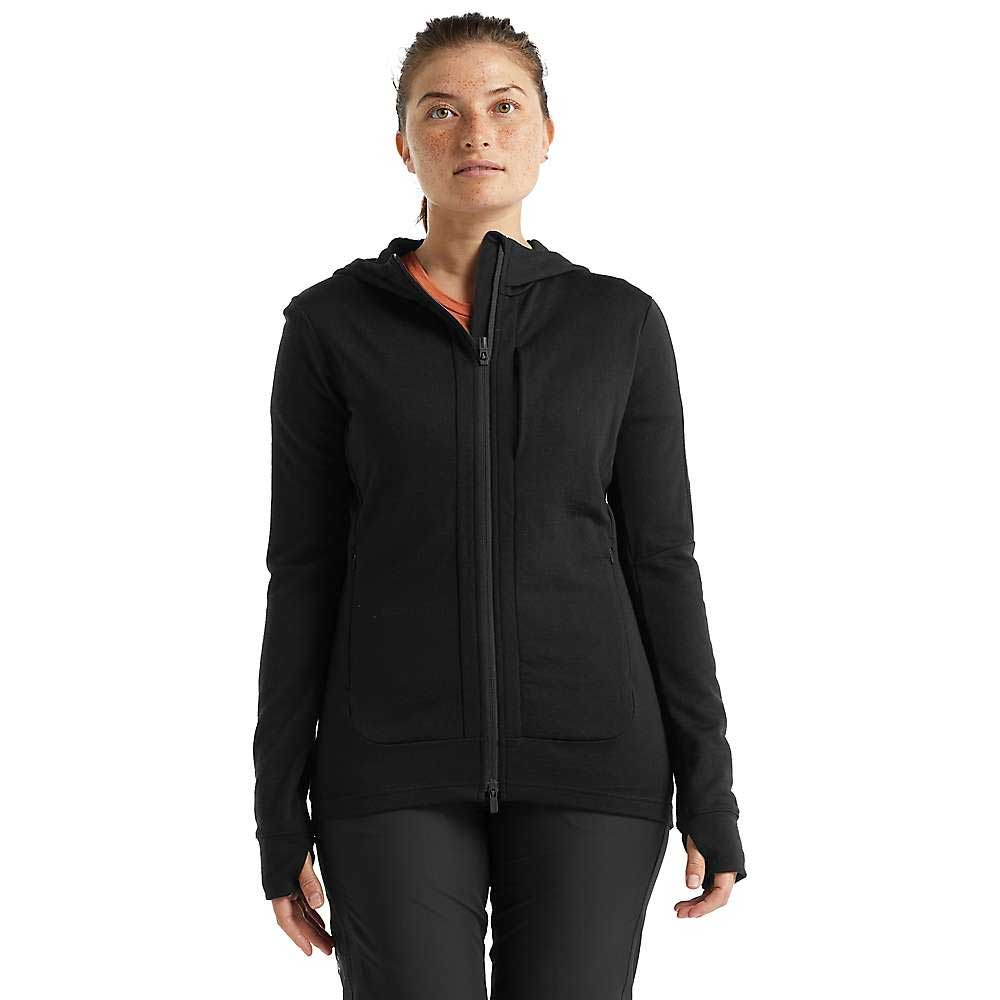 A person faces forward wearing the Icebreaker Womens Quantum III LS Zip Hoodie in black with a hood and front pockets, paired with black pants, against a completely white background.