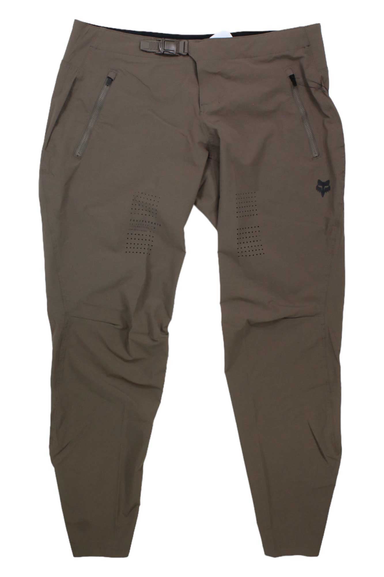 The Fox Womens Flexair Pant, shown laid flat on a white background, are brown tapered athletic mountain bike pants featuring zippered pockets, thigh perforations for ventilation, moisture-wicking fabric, an adjustable waist buckle, and a black logo.