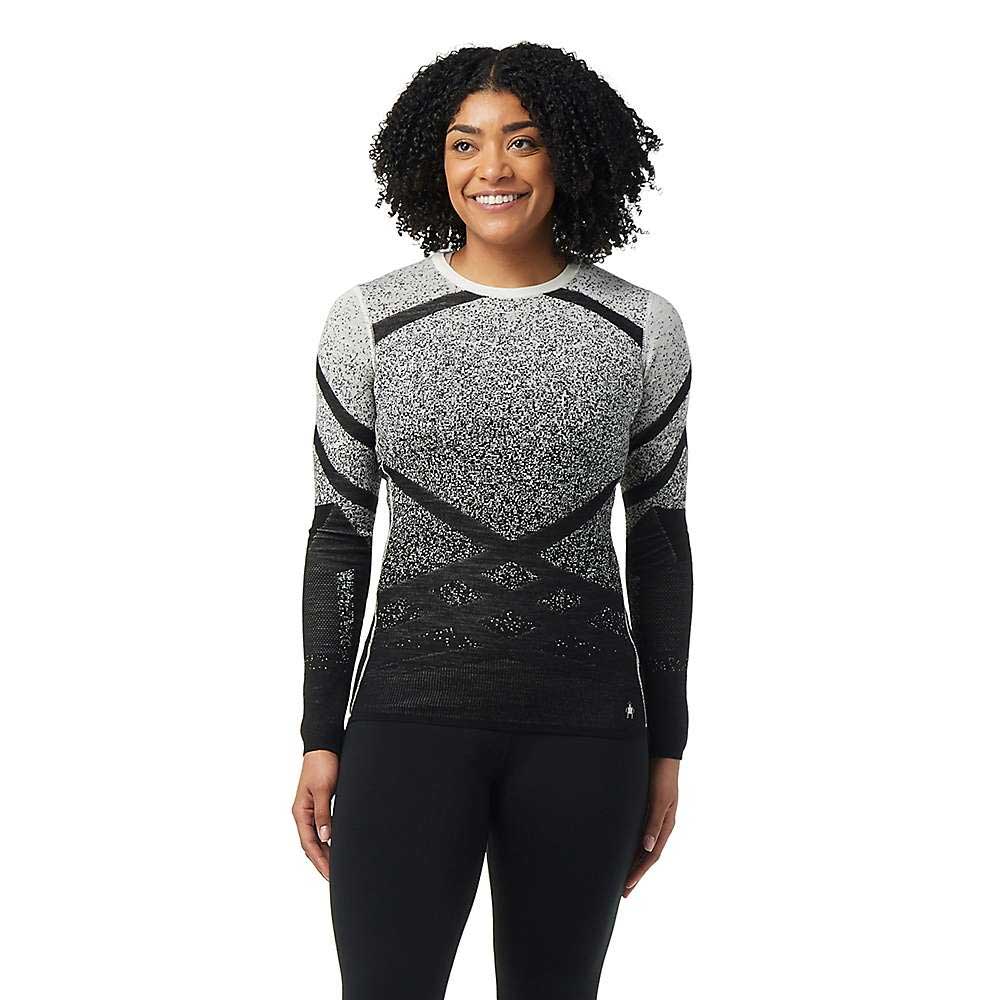 A woman with curly hair smiles wearing the Smartwool Womens Intraknit Thermal Merino Base Layer Pattern Crew and black leggings, standing against a white background.