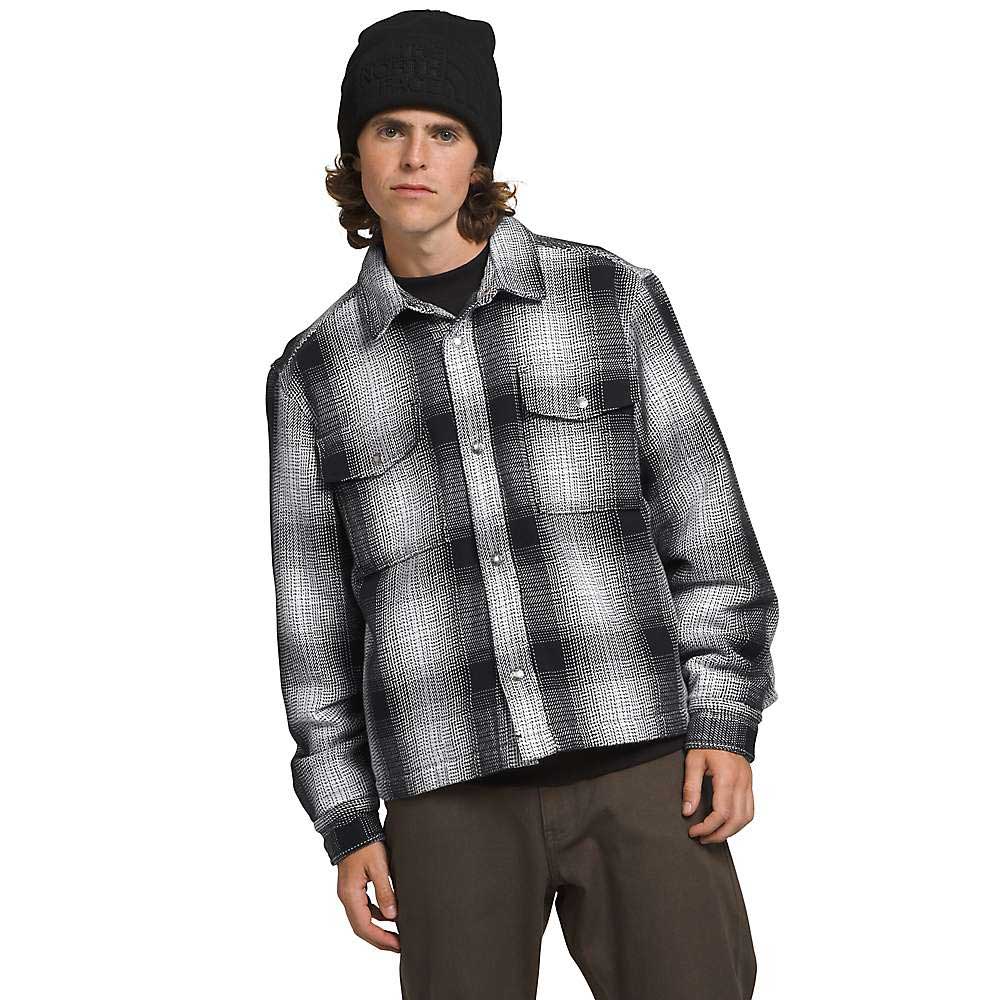 A young man in a black beanie and dark pants wears The North Face Men's Valley Twill Utility Shacket in black and white plaid, standing against a plain white background and looking at the camera with a neutral expression.