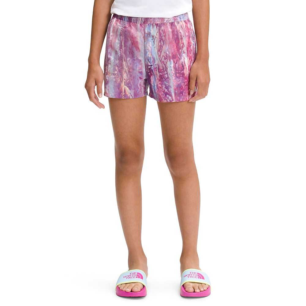 A person is wearing The North Face Girls Printed Amphibious Class V Water Short in pink and purple, a white shirt, and white slide sandals with pink soles. The image focuses on their legs and waist against a white background.