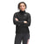 A woman stands facing the camera, arms crossed, wearing The North Face Women's ThermoBall Eco Jacket with a high collar and zip front. Made from recycled nylon with synthetic insulation, it features a small white chest logo.