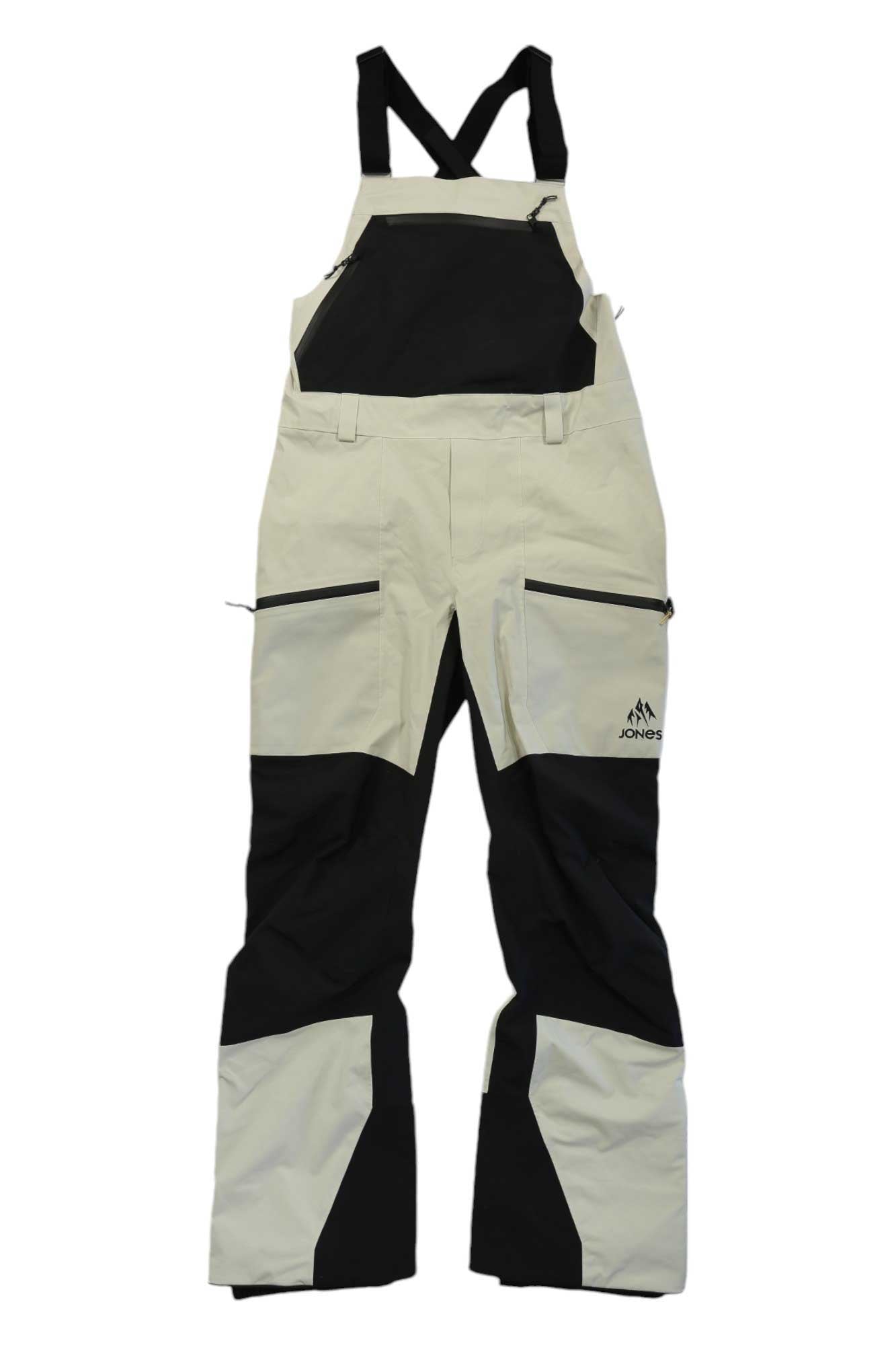 The Jones Womens MTN Surf Recycled Bib Pant is a beige and black waterproof bib with adjustable straps, zippered pockets, reinforced knees, side venting, and the Jones logo on the left thigh.