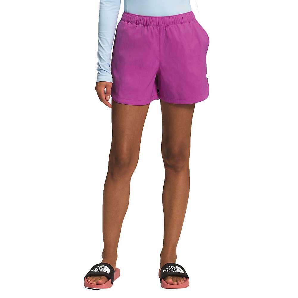 A person stands against a white background wearing a light blue long-sleeve top, black sandals with white text, and The North Face Women's Class V Short in bright pink. Their hands are in their pockets and the shorts have a relaxed fit.