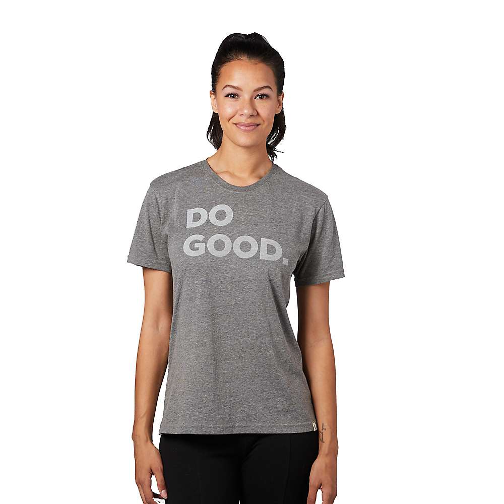 A woman with dark hair in a ponytail smiles while wearing the Cotopaxi Womens Do Good SS Tee, a gray organic cotton shirt with bold white DO GOOD text, standing against a plain white background.
