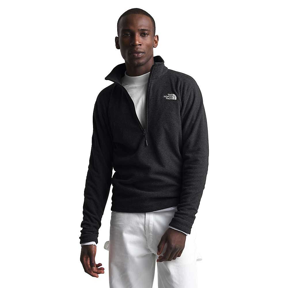 A man stands against a plain white background wearing The North Face Mens Textured Cap Rock 1/4 Zip Fleece in black over a white shirt and white pants.