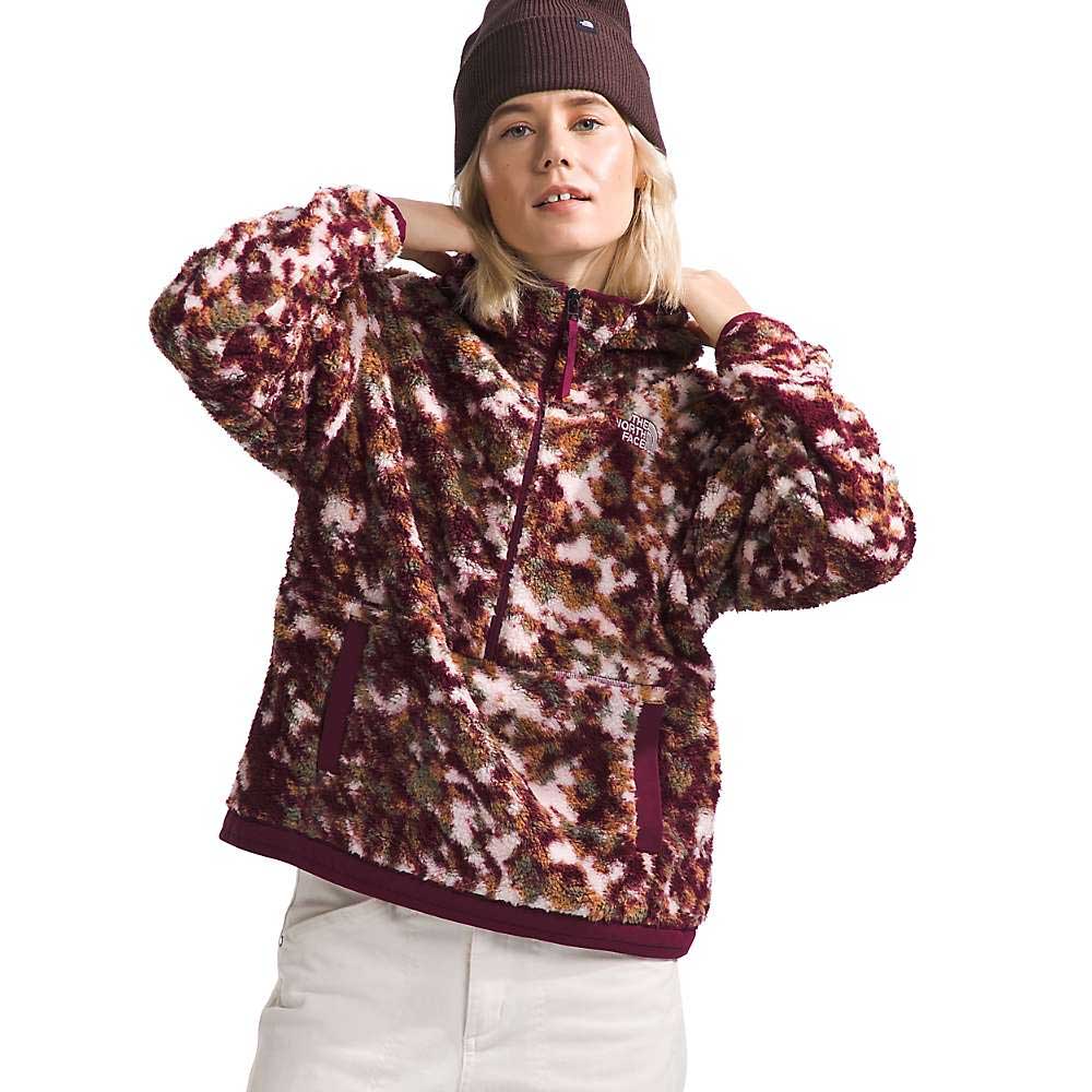 A woman confidently adjusts the collar of The North Face Womens Campshire Fleece Hoodie in maroon and white, paired with white pants and a brown beanie, while looking at the camera.