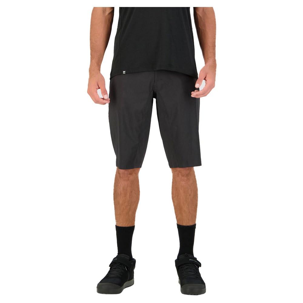 A person faces forward in a black t-shirt, Mons Royale Virage Men's Bike Shorts Black XL, black socks, and black sneakers against a white background. The person's face is not visible.