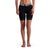 A person stands barefoot, wearing Mons Royale Women's Enduro Bike Short Liner in black with a wide elastic waistband featuring MONS ROYALE in white; the upper body is not visible.