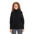 A woman with long curly red hair, smiling against a plain white background, wears the Icebreaker Women's Seevista Funnel Neck Sweater in black and gray pants.
