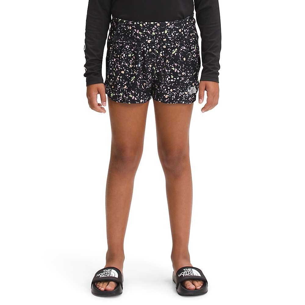 A child in a black long-sleeve shirt, The North Face Girls Printed Amphibious Knit Class V 3 Inch Short with a floral pattern, and black slide sandals stands facing forward against a plain white background.