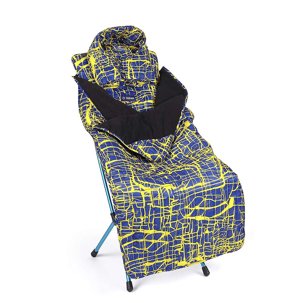 The Helinox Toasty Blanket for Sunset/Beach, featuring blue and yellow patterns, is draped over a foldable camping chair, offering insulated warmth and comfort for outdoor use.