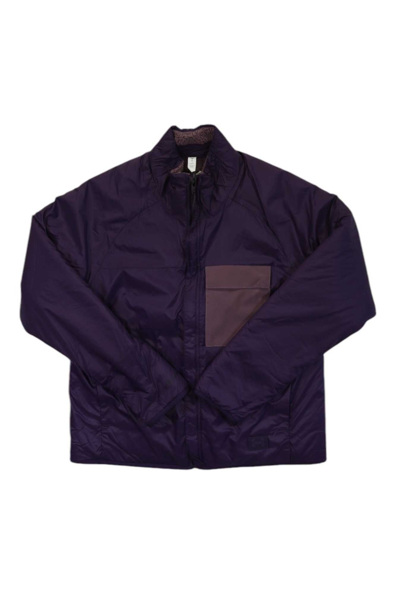 A dark purple Under Armour Womens Latitude Reversible Full Zip Jacket with long sleeves, a collar, and front zipper. It has a light purple left chest pocket and is laid flat with crossed sleeves.