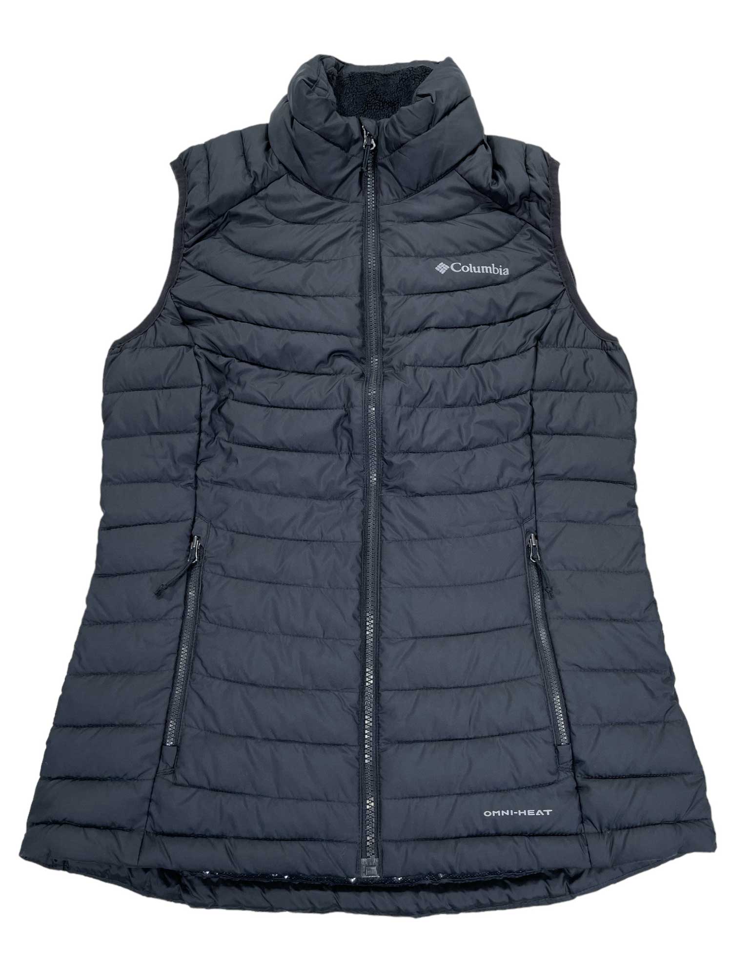 The Womens White Out Vest by Columbia is a black, sleeveless insulated vest with horizontal quilting, high collar, zippered front and pockets, ideal for hiking. The Columbia logo appears on the left chest.