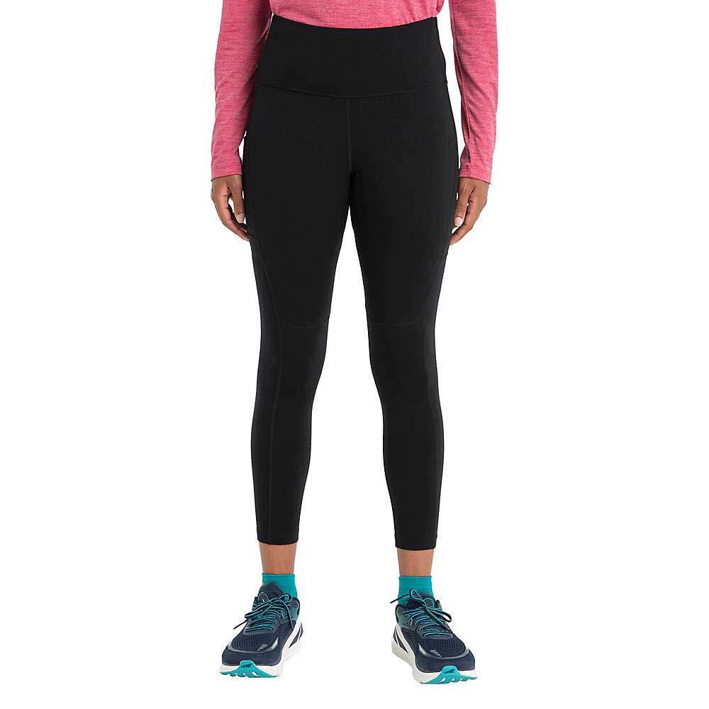 A person wearing a long-sleeve pink top, Icebreaker Womens Merino Speed Winter Tight in black, and teal and black athletic shoes stands against a plain white background. The image shows them from shoulders to feet.