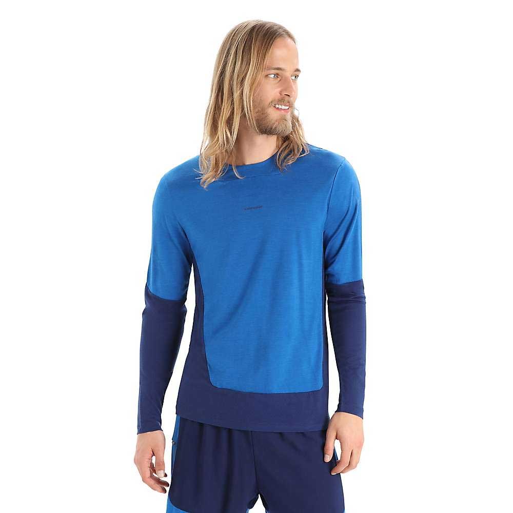 A man with long blond hair and a beard is wearing the Icebreaker Mens Zoneknit LS Tee in two-tone blue athletic style, paired with matching shorts, standing and looking left against a plain white background.