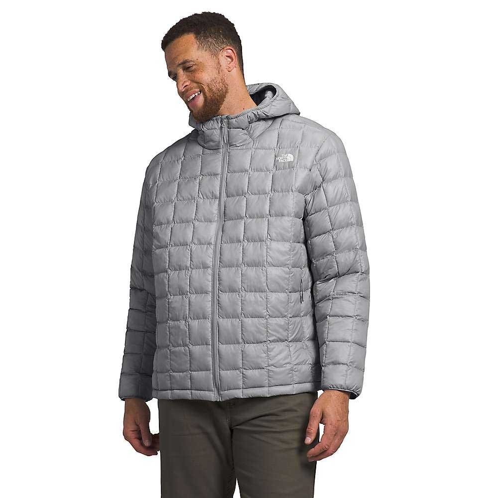 A man smiles and looks to the side wearing The North Face Men's Big Thermoball Eco 2.0 Hoodie in light gray, featuring a square quilted design made from recycled nylon, paired with casual brown pants.
