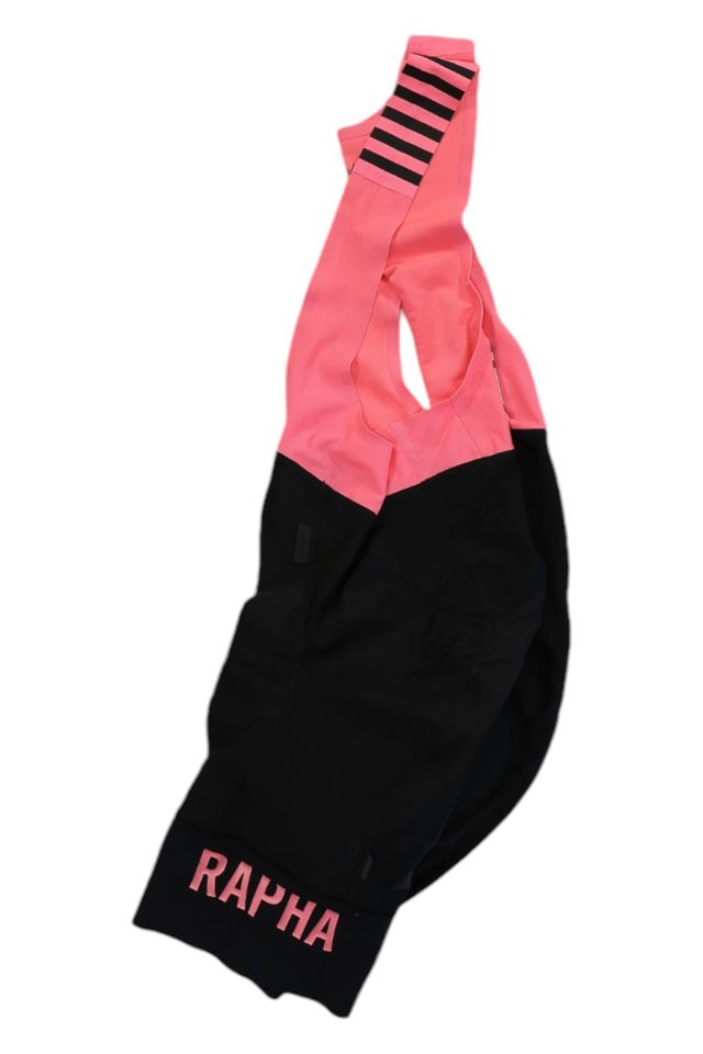 The Rapha Mens Pro Team Bib Shorts II - Regular feature pink straps and upper section, black lower half, and pink RAPHA logo on one leg cuff. These cycling bib shorts include a race-grade chamois for optimal comfort.