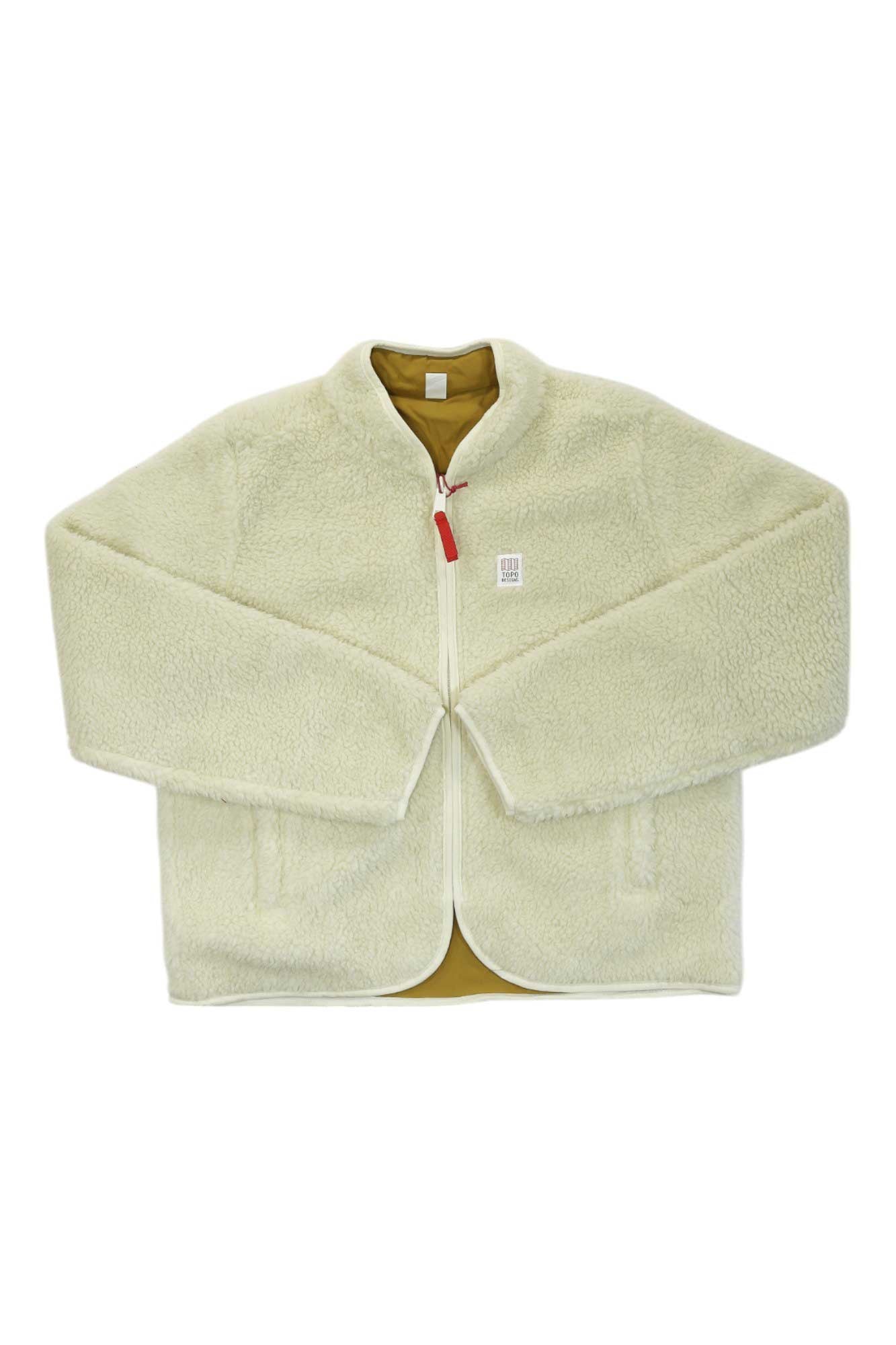 The Topo Designs Womens Sherpa Jacket is cream-colored with long sleeves, a white zipper and trim, red zipper pull, two front pockets, and light brown lining—great for outdoor adventures. Shown laid flat on a white background.