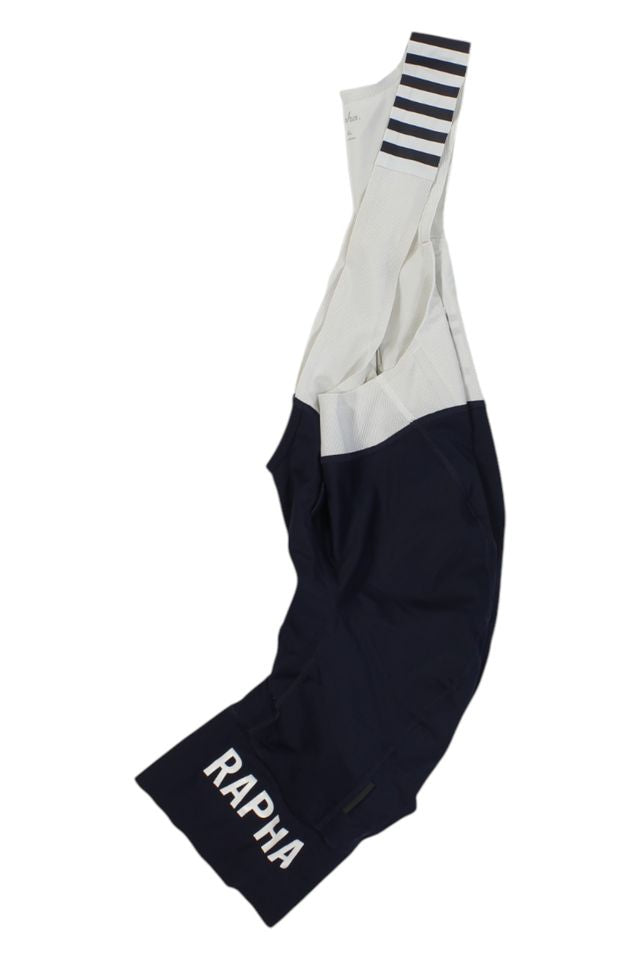 Rapha Mens Pro Team Bib Shorts II - Regular in navy and white with race-grade chamois, RAPHA in white on the left leg, and black-and-white striped shoulder straps, shown on a white background.