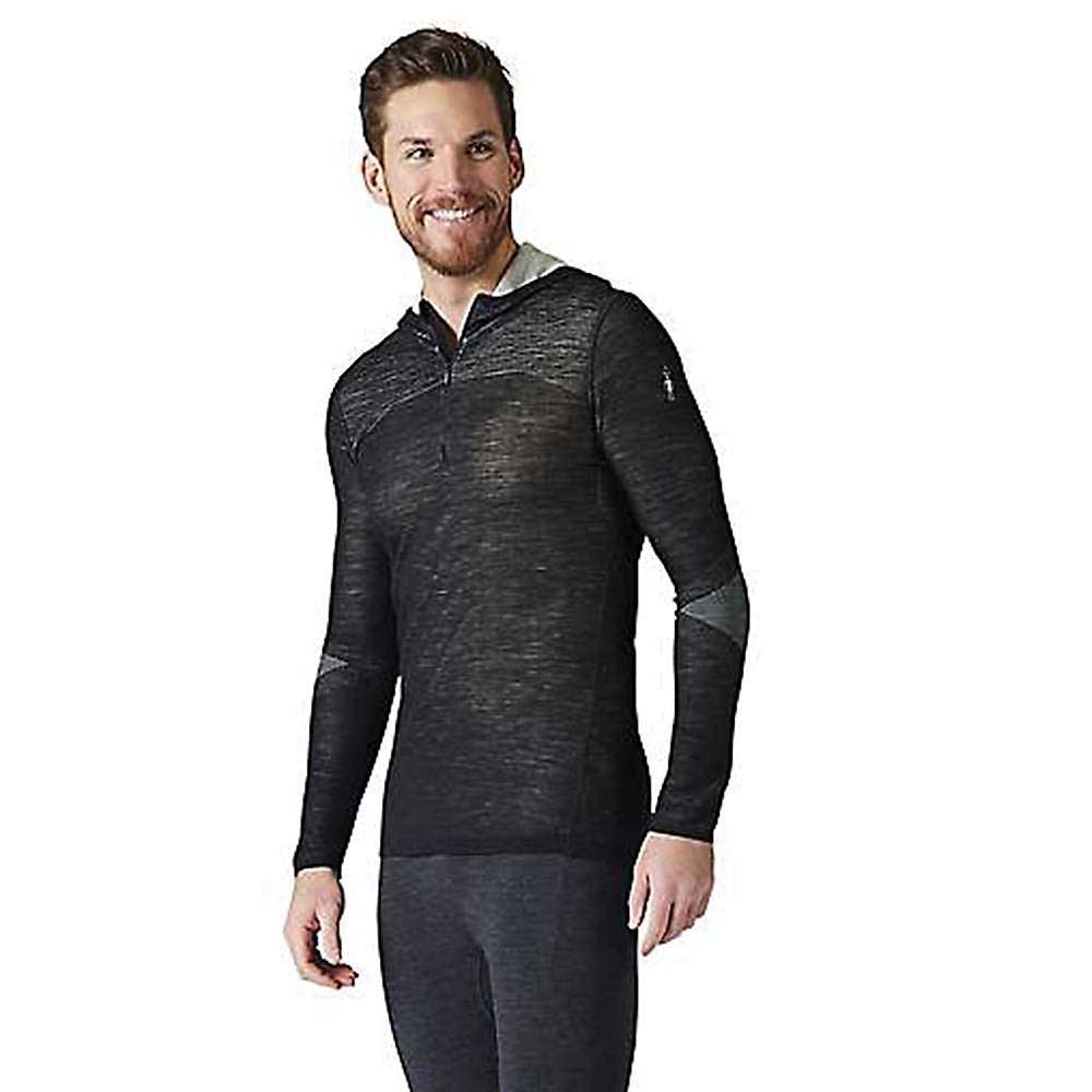 A man with short brown hair and a beard smiles, wearing the Smartwool Mens Intraknit Merino 200 1/2 Zip Hoodie with grey accents and dark leggings, ideal for men’s snowsports, standing against a plain white background.