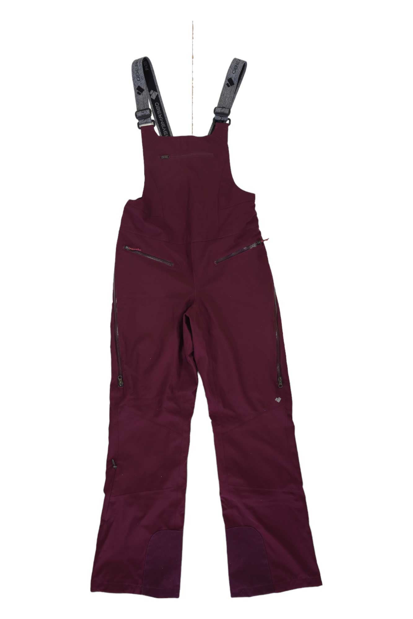 The maroon Obermeyer Womens Bliss Bib Pant features black adjustable straps, multiple zippered chest and leg pockets, and reinforced knee patches—perfect waterproof bibs for winter adventures, shown laid flat on a white background.