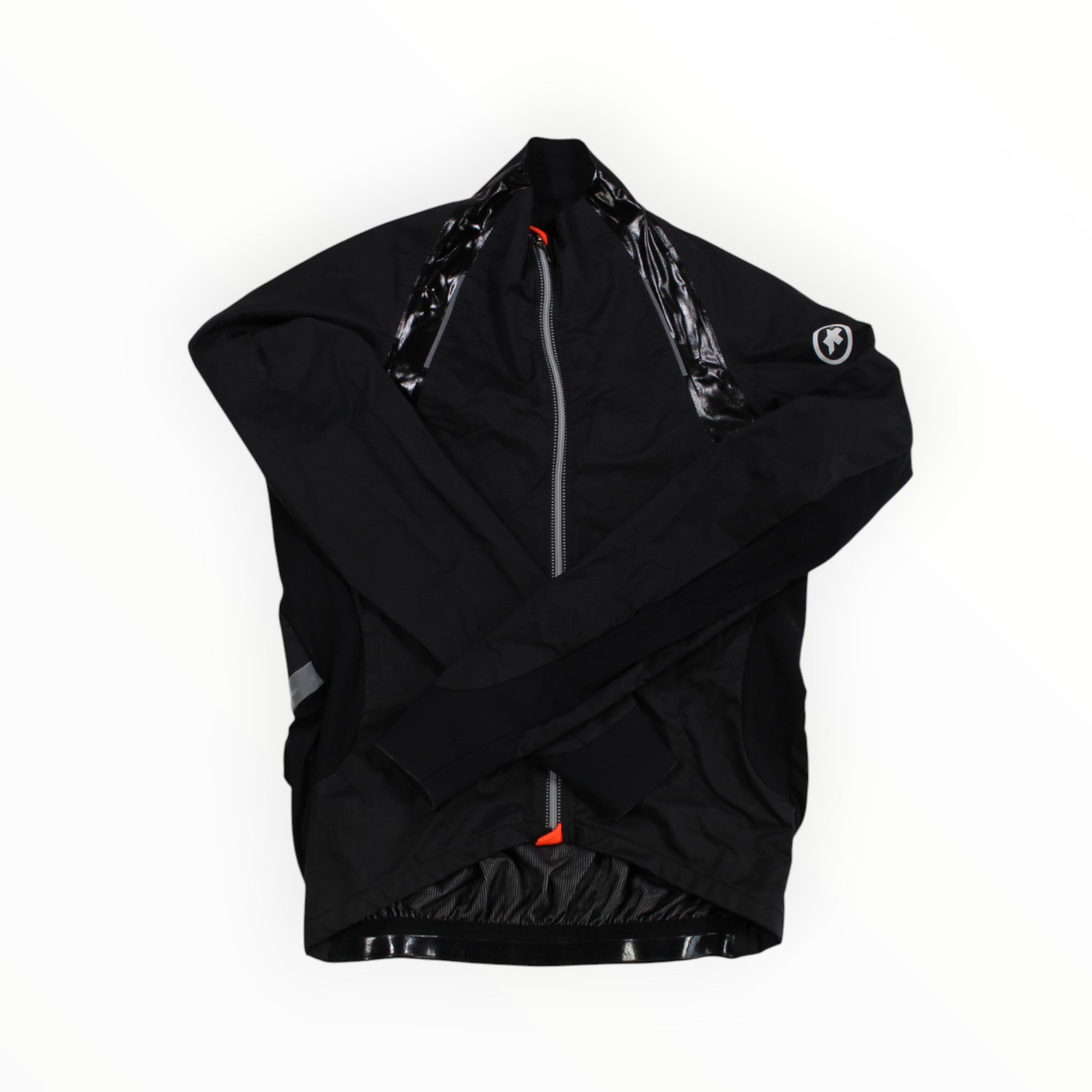 The Assos Mens RS Sturmprinz Jacket is shown in black with a glossy zipper trim, small shoulder logo patch, and orange inner accents, lying flat on a white background. This windproof cycling jacket combines style and performance.