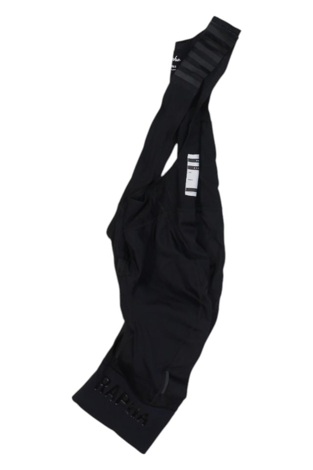 A pair of black Rapha Mens Pro Team Bib Shorts II - Regular featuring RAPHA branding on the leg, shoulder straps, a white inner care label, and a race-grade chamois for enhanced comfort during intense rides.