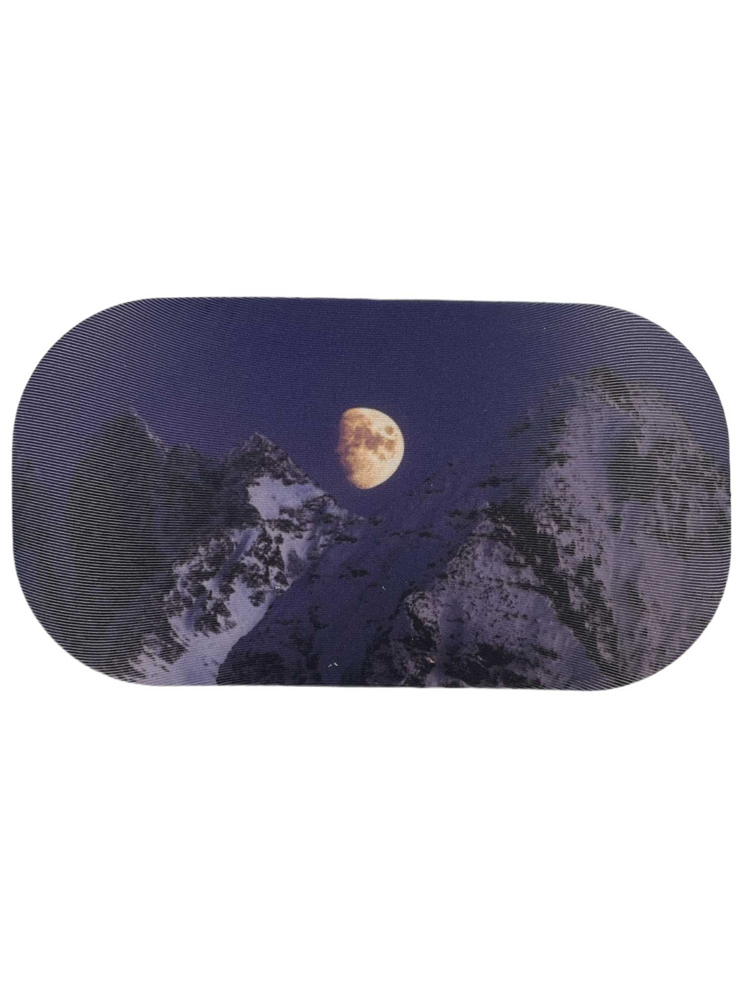 A bright full moon illuminates snow-capped peaks as it reflects off a GoggleSoc Protective Goggle Cover lying on the snowy ground.