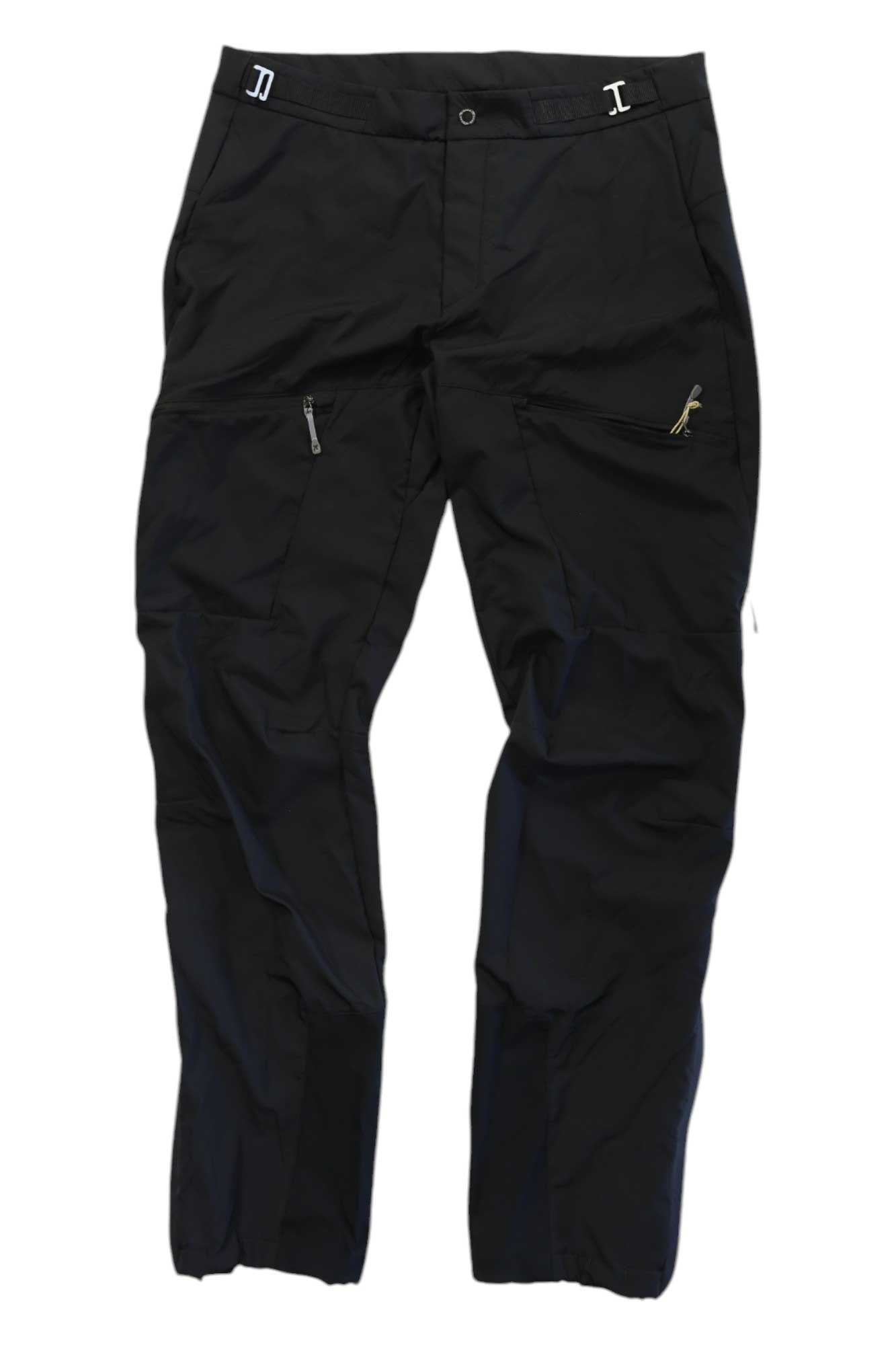 A pair of Houdini Mens Pace Pants in black, featuring zippered pockets and a small yellow embroidered animal logo on the upper left thigh, displayed flat on a white background.
