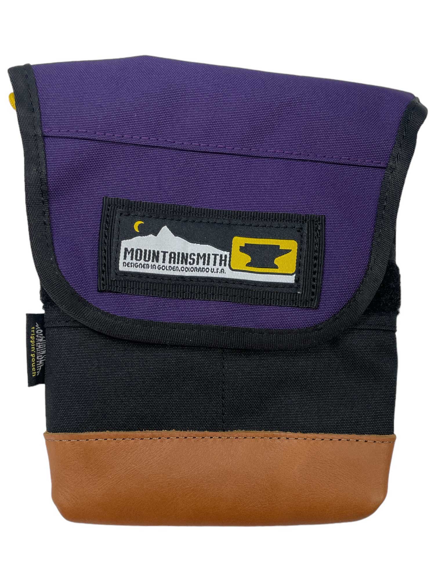 The Mountainsmith Trippin Pouch Waistpack is a compact crossbody with a purple flap, black body, and brown leather bottom. A yellow and black logo patch accents the front, giving it a simple, rugged style.