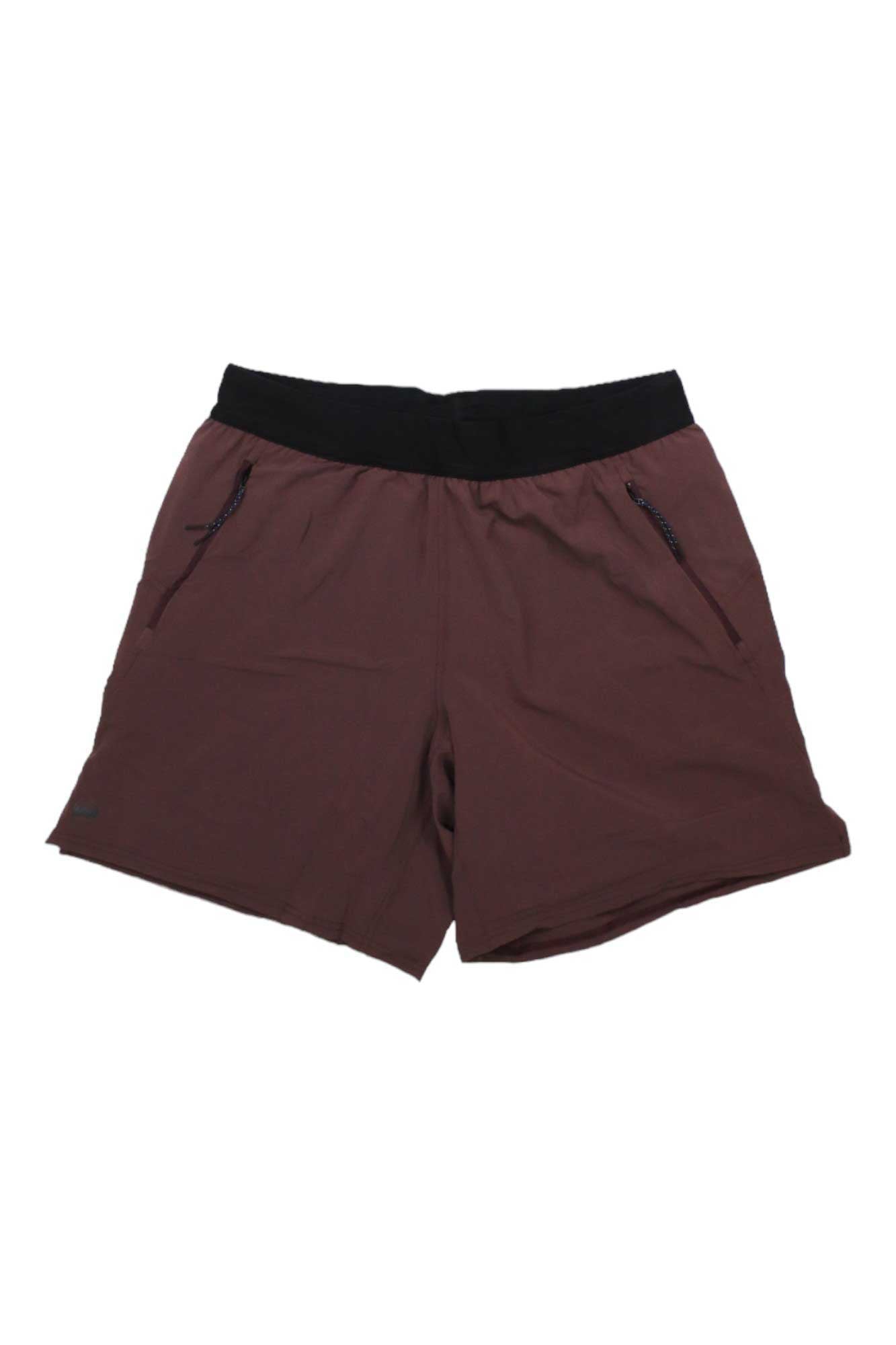 The Janji Men's 7 Inch AFO Traverse 2-in-1 Short in maroon features a black elastic waistband, zippered side pockets, and a built-in compression liner, shown laid flat on a white background.