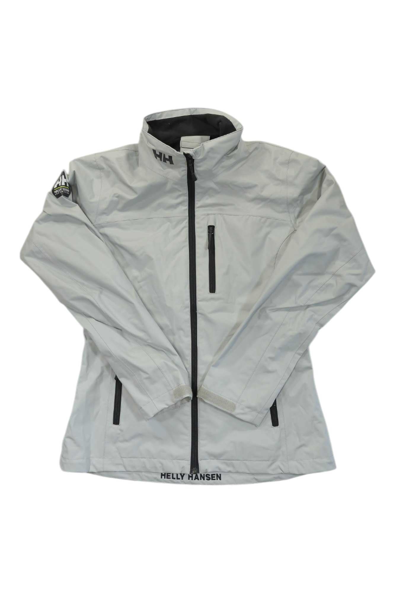 The Helly Hansen Women's Crew Jacket is light gray with a high collar, black front zipper, two vertical zippered pockets, and Helly Hansen logos on the collar and hem. This waterproof jacket has a patch on the left sleeve.